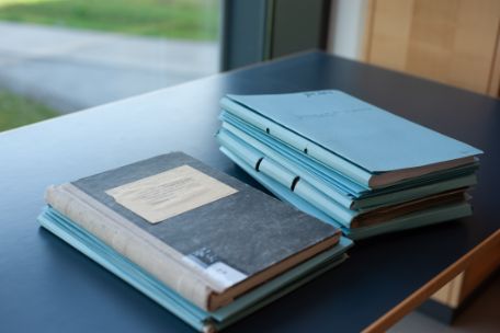 On a table are an old notebook and a stack of blue folders.