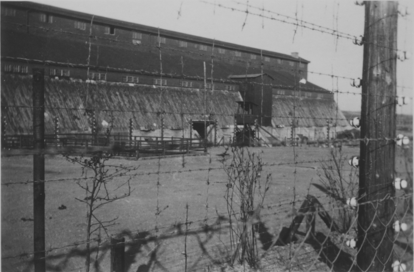 View through the barbed wire fence to the field barn converted into prisoner accommodation.