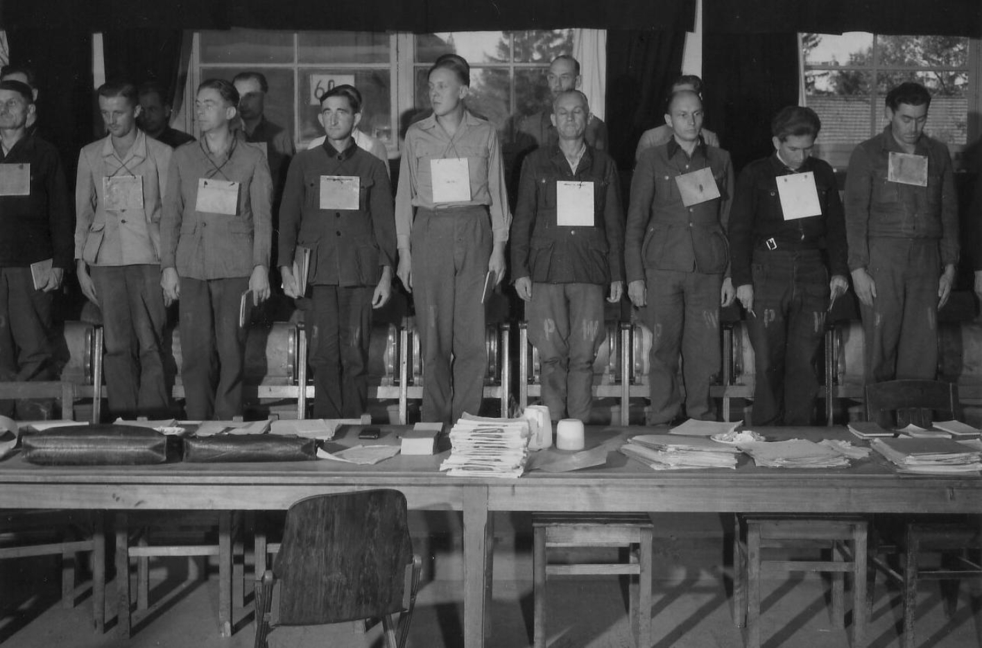A photo of the defendants standing on their chairs. They all have a sign hanging around their necks with their name and charges listed.