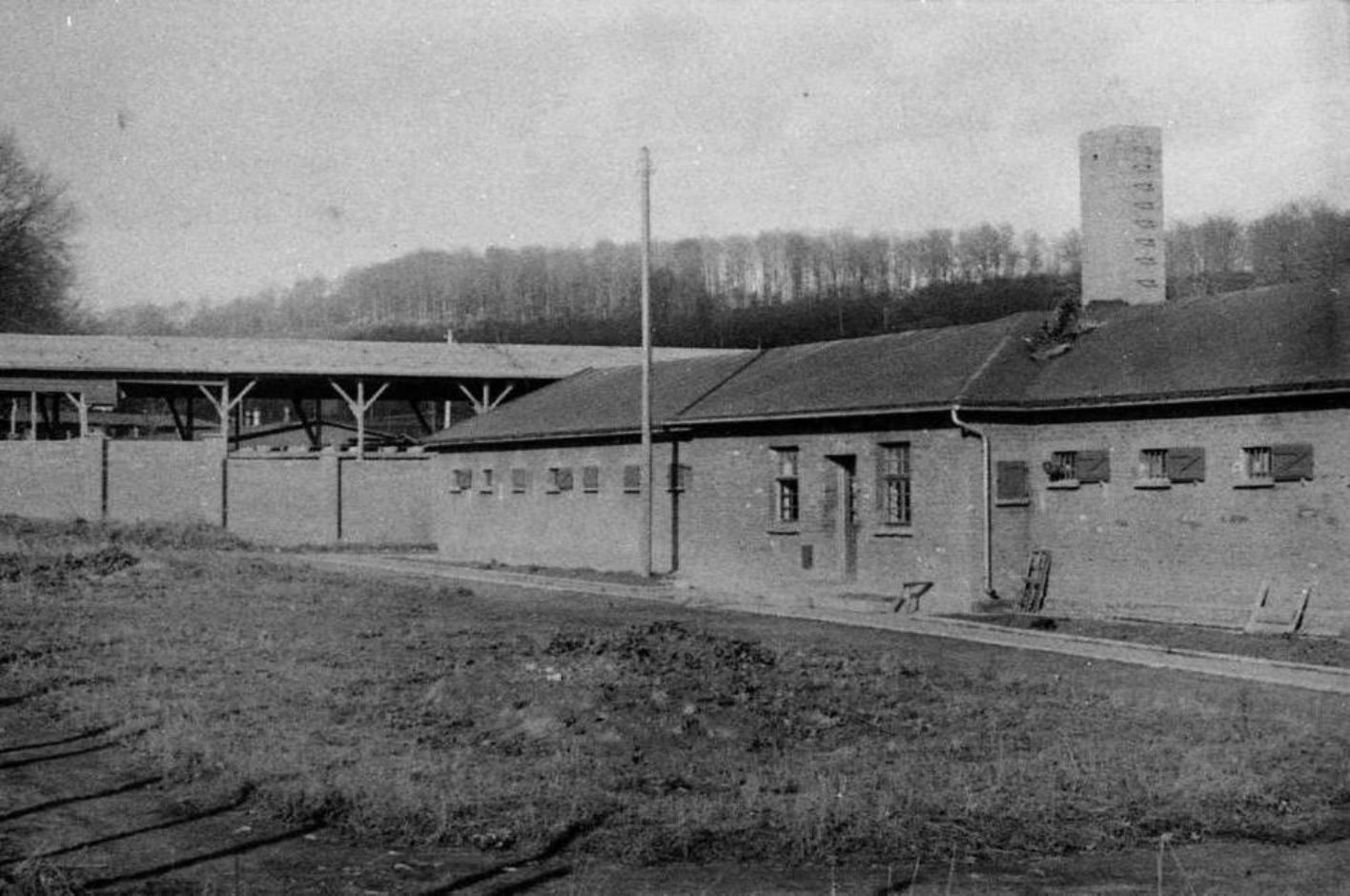 View of the prison cell building with barred windows. On the left in the background a storage shed belonging to the wood yard.