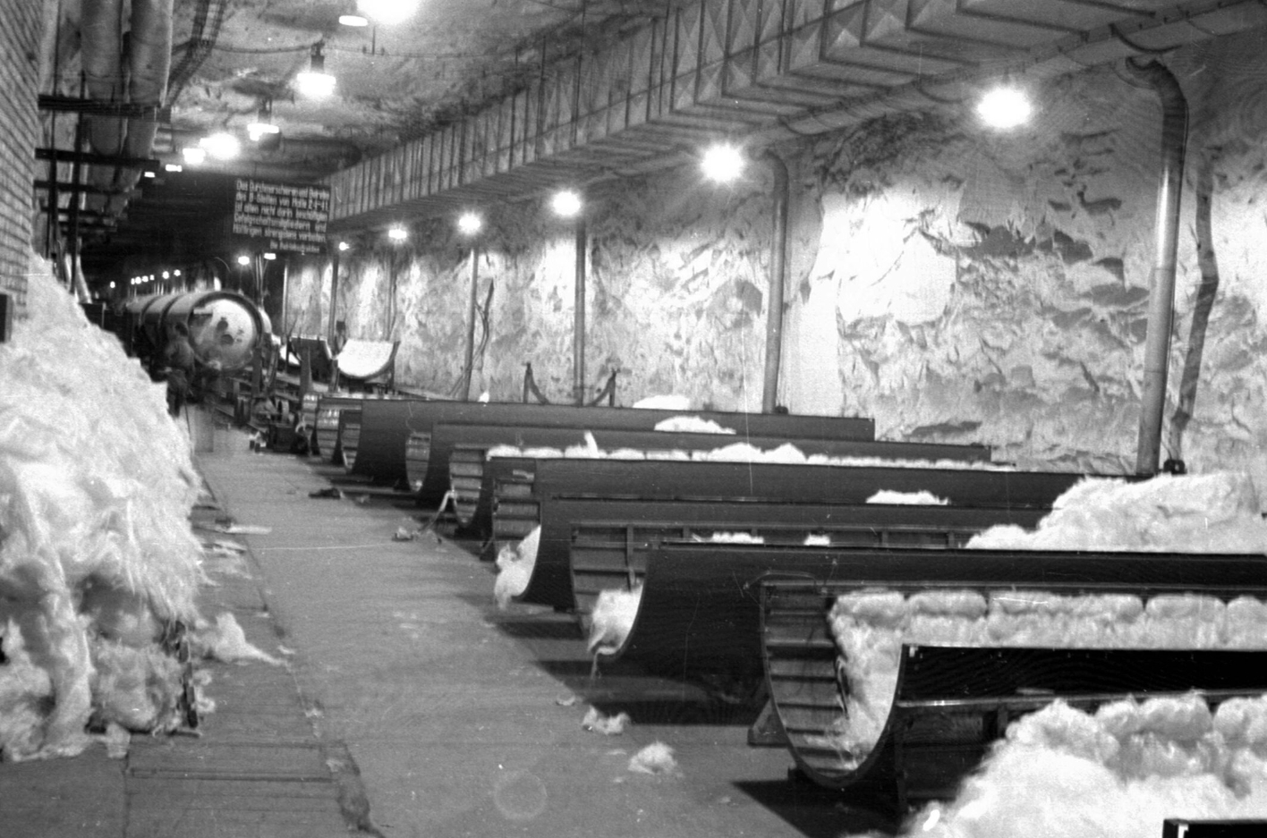 You can see a driving tunnel. Piles of glass wool lie on the left. On the right along the tunnel, V2 half-shells padded with glass wool are arranged at regular intervals.