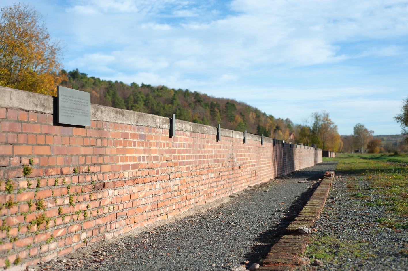 This photo shows the information and memorial site at the subcamp at the former camp station. It is a long brick foundation to which metal plaques have been attached at regular intervals.