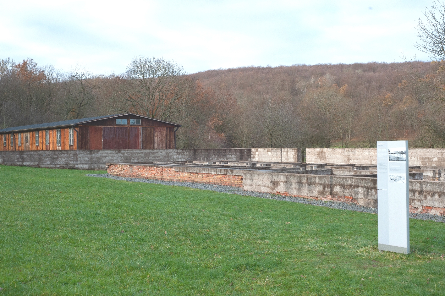 An information stele can be seen in the right foreground of the picture, which reveals that it is the location of the former camp prison. The foundation walls can be seen behind it. The carpentry barracks can be seen in the background.