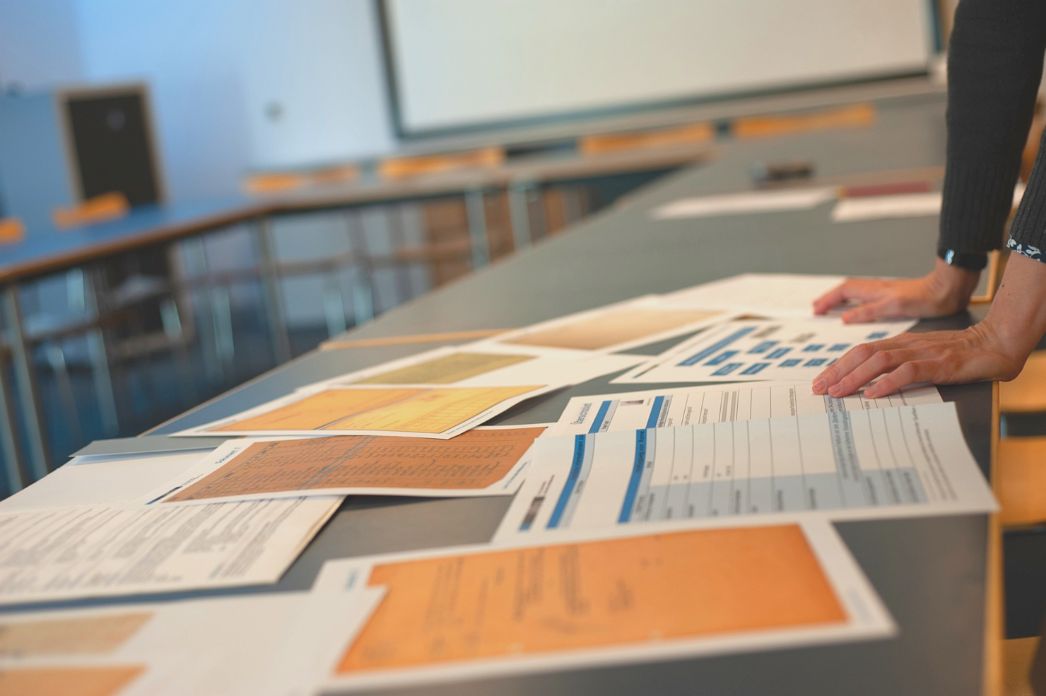 Examples of documents prepared for work with groups lie on a table in a seminar room. On the right, the hands of a woman can be seen leaning on the table.