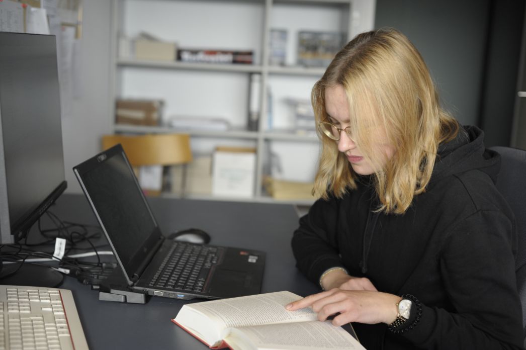 Eine junge Freiwilligendienstleistende sitzt an ihrem Arbeitsplatz und ist in ein Buch vertieft.