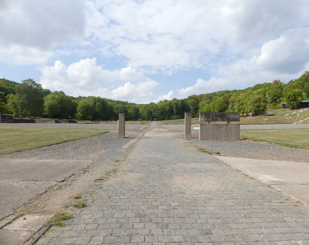 The picture shows an open area. Some areas are overgrown with grass. Other areas are covered with gravel. In the center of the picture, about 10 meters away, there are 2 concrete pillars. 