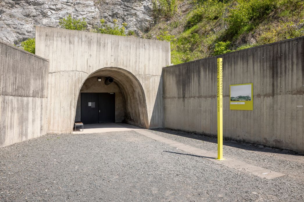 Der Eingang zum Stollen führt in einen Berg. Der Eingang hat rechts und links dicke Betonwände.