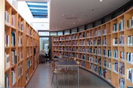 Zu sehen ist der Bibliotheksraum, der durch eine gerade verlaufende Regalwand auf der linken Seite und eine geschwungene auf der rechten Seite begrenzt wird.