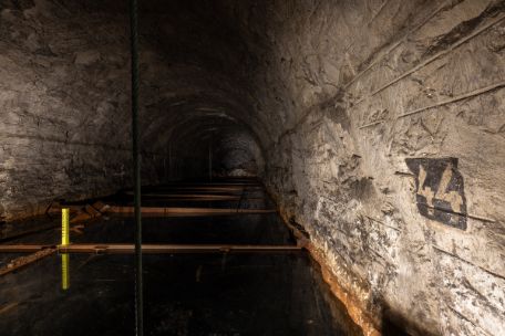 Das Foto zeigt die mit Grundwasser überflutete Kammer 44. An der Wand rechts ist eine 44 zu sehen. Inmitten des Wassers steht eine kleine gelbe Stele.