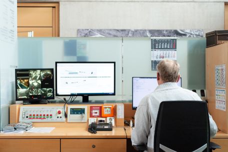 Eiin Mitarbeiter der Information sitzt an seinem Schreibtisch. Er ist dem Fotografen mit dem Rücken zugewandt und blickt auf mehrere Bildschirme.