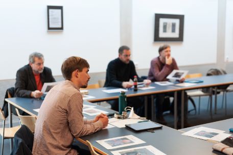 Das Foto zeigt den Seminarraum während der Durchführung eines Seminars. Insgesamt sind vier Männer zu erkennen, die in vor sich liegendes Bildungsmaterial vertieft sind oder miteinander diskutieren.
