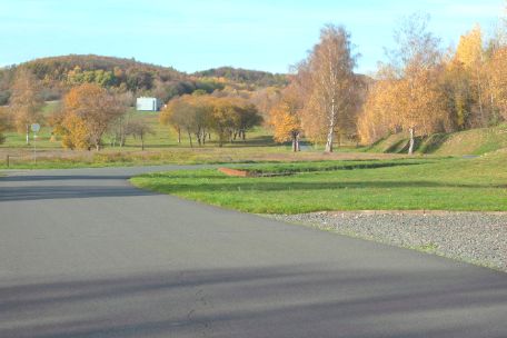 Rechts im Bild steht ein Kleines Mauerstück aus rotem Ziegelstein. An diesem Mauerstück ist eine Tafel mit einer Karte angebracht, auf der die Route der Todesmärsche vom KZ Mittelbau-Dora aus verzeichnet sind. 