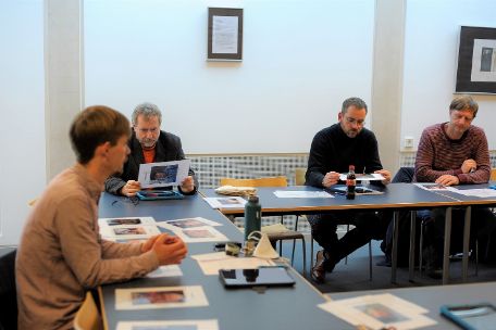 Das Foto zeigt den Seminarraum während der Durchführung eines Seminars. Insgesamt sind vier Männer zu erkennen, die in vor sich liegendes Bildungsmaterial vertieft sind, oder miteinander diskutieren.