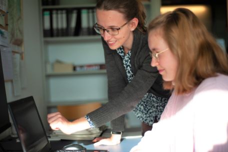 A staff member at the Mittelbau-Dora Concentration Camp Memorial shows a young volunteer something on a laptop.