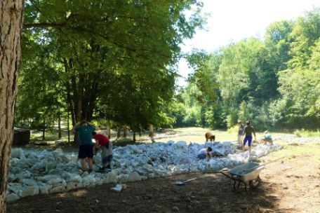 Young people working in a wooded area arranging light colored stones in certain shapes.