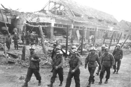 Sieben amerikanische Soldaten auf dem Weg vor den zerstörten Fahrzeug-Garagen des Aussenlagers Boelcke-Kaserne. 
