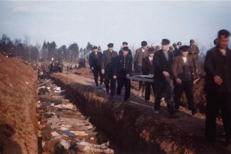 Einwohner aus Nordhausen beerdigen unter Aufsicht amerikanischer Soldaten die Toten des KZ-Aussenlagers Boelcke-Kaserne in einem Reihengrab. Rechts am Graben tragen einige Männer eine Trage mit einem toten Körper vorbei. Der Graben ist dicht an dicht gefüllt mit Leichen.