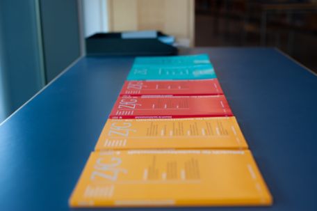 Auf einem Tisch in der Bibliothek liegen 6 geschichtswissenschaftliche Zeitschriften. Die vorderen zwei sind Gelb, die dahinter rot und die letzten zwei blau.