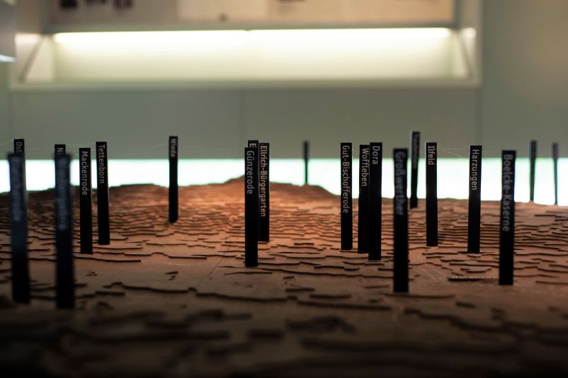 A three-dimensional relief map made of wood. Individual locations are labeled with vertical black bars. 