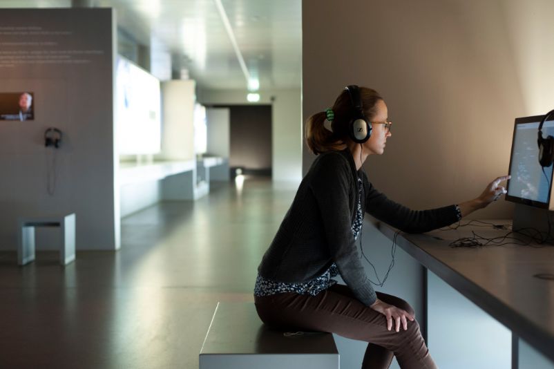A visitor sits at a listening station wearing headphones. 