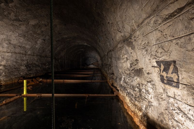 The photo shows chamber 44, which is flooded with groundwater. A 44 can be seen on the wall on the right. A small yellow stele stands in the middle of the water.