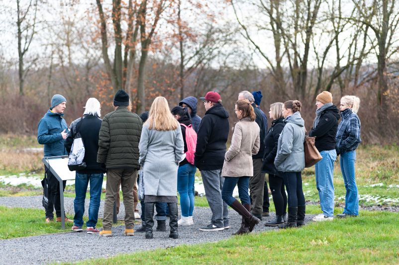 A group of memorial visitors stands around their tour guide and listens.