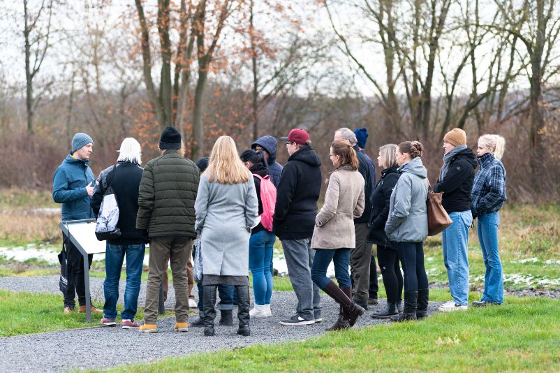 Eine Gruppe Gededenkstättenbesucher:innen steht um ihren Runggangsbegleiter herum und hört ihm zu.