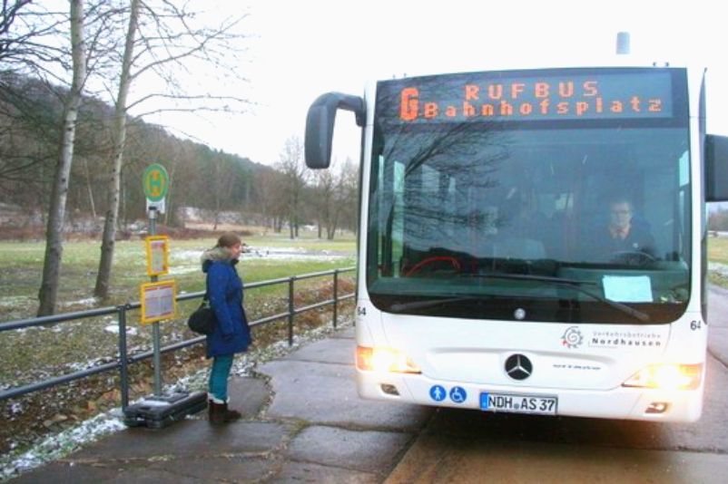 Eine Bushaltestelle. Daneben ein Bus, der mit "Rufbus" beschriftet ist. 