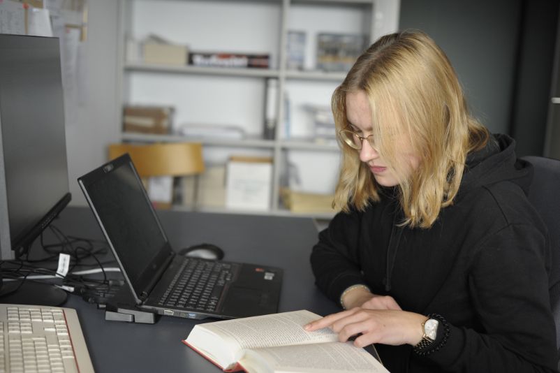 A young volunteer sits at her workstation, engrossed in a book.