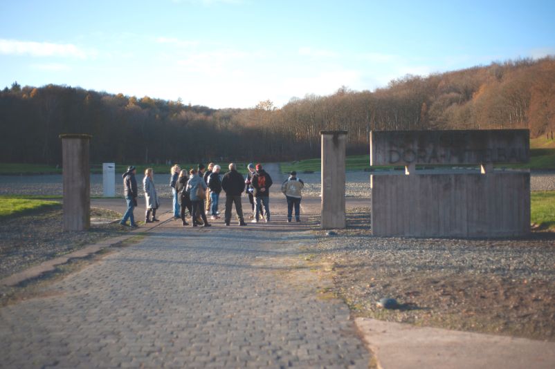 A group stands between the concrete pillars that mark the entrance to the former prisoners' camp.