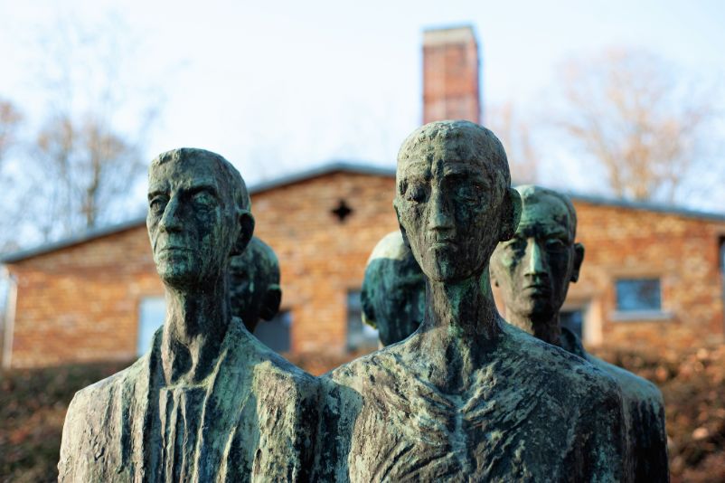 Das Foto zeigt die Gesichter einer Figurengruppe, die vier Häftlinge darstellt, die in Zweierreihe stehen. Ihre Gesichter sehen traurig und eingefallen aus.