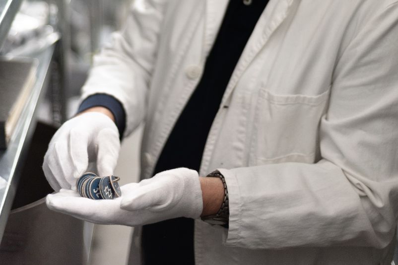 The head of the collection of the Mittelbau-Dora concentration camp memorial Torsten Heß, presents a few dog tags from the collection. He wears white gloves and a lab coat.