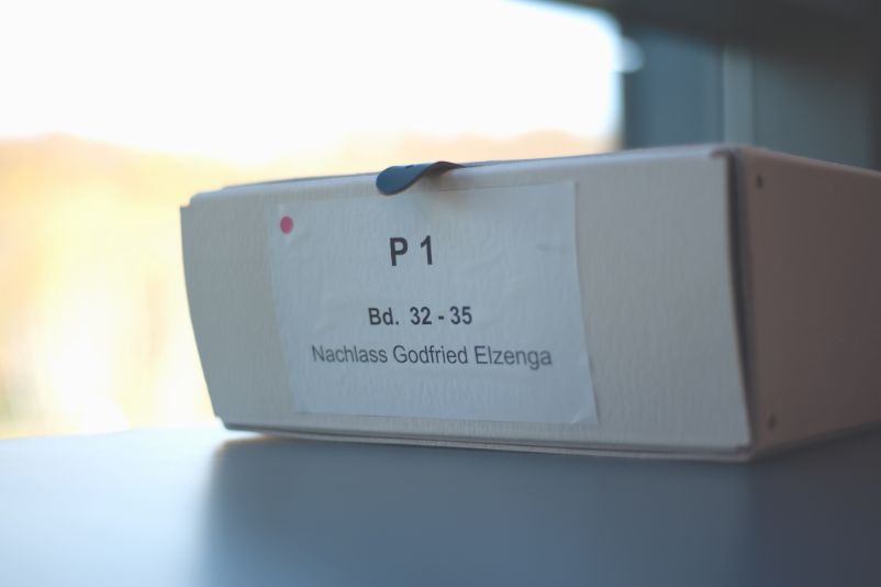 Auf einem Tisch liegt ein Karton mit der Ausfrift: " P1, Bd. 32-35, Nachlass Gottfried Elzenga".