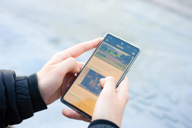 A person holding a smartphone on which the app of the Mittelbau-Dora concentration camp memorial is open.